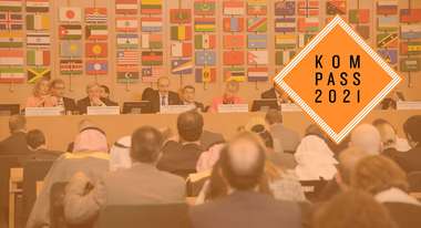 FAO-Treffen in Rom – Federica Mogherini, António Guterres und weitere Politiker*innen sitzen auf einem Podium. Im Hintergrund sind Flaggen vieler verschiedener Länder zu sehen. Rechts oben ist das Kompass 2021 Logo. 