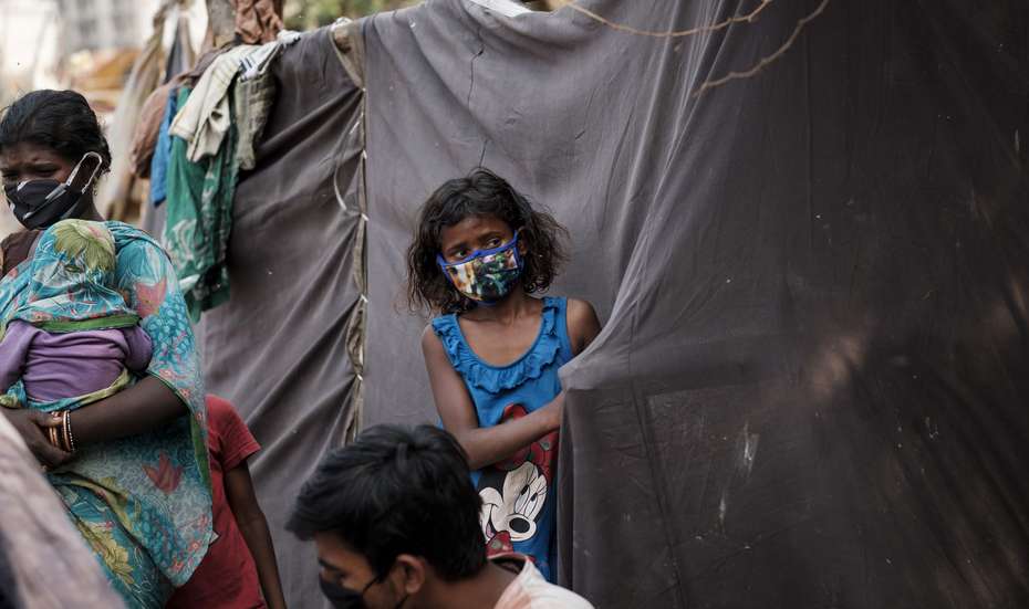 Ein Mädchen mit Mundschutz steht an einem Zelt aus schwarzen Planen.