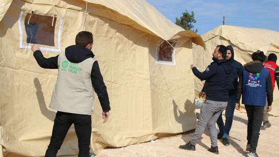 Männer stellen große Zelten als Notunterkunft für Familien auf