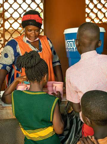 Eine Frau gibt Trinkwasser aus einem Keramikfilter an Kinder aus.