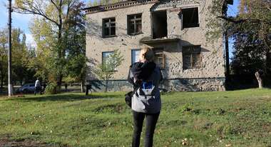 Eine Frau steht vor einem zerstörten Haus, Ukraine 2022.