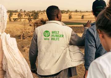 Ein Mitarbeiter der Welthungerhilfe zeigt in die Landschaft. Er ist von hinten zu sehen und trägt eine Weste mit dem neuen Logo der Welthungerhilfe.