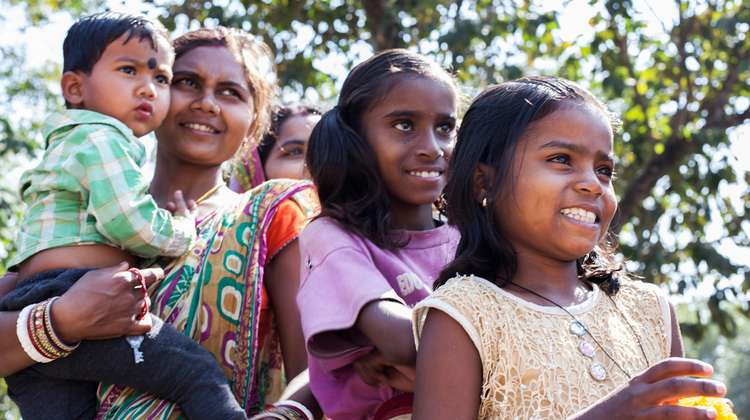 Eine Frau im Sari mit einem Kind auf dem Arm. Neben ihr zwei Mädchen, alle lachen.