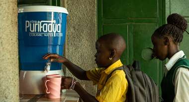 Kinder nehmen sauberes Wasser aus einem Keramikfilter.