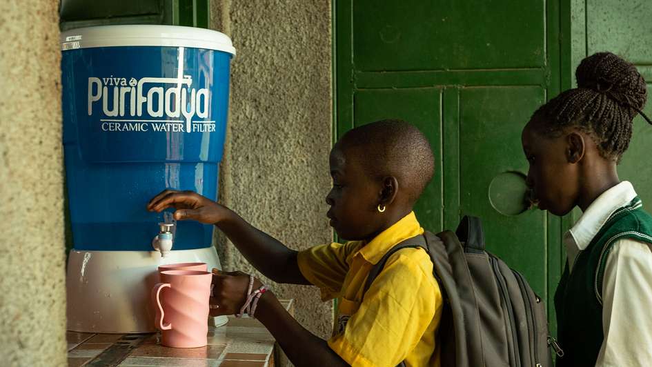 Kinder nehmen sauberes Wasser aus einem Keramikfilter.