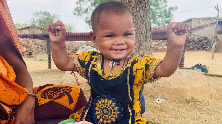 Ein Kind lacht und hebt die Arme hoch, Indien 2021.