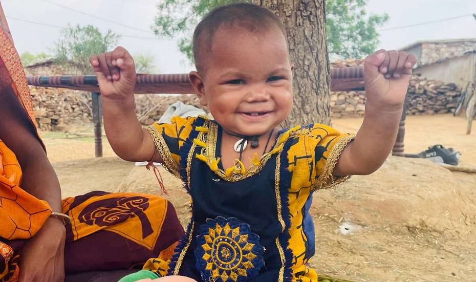 Ein Kind lacht und hebt die Arme hoch, Indien 2021.