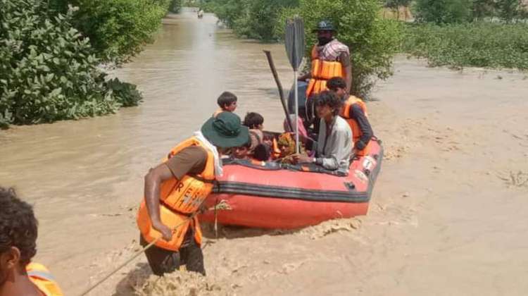 Überschwemmungen in Pakistan. Männer ziehen ein rotes Rettungsboot, in dem mehrere Menschen sitzen, durch schmutziges Wasser