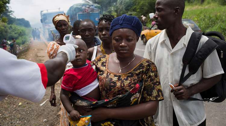 Coronavirus in Afrika. Bild: Eine Frau trägt ihr Kleinkind auf dem Arm. Jemand anderes misst, ob das Kind Fieber hat.