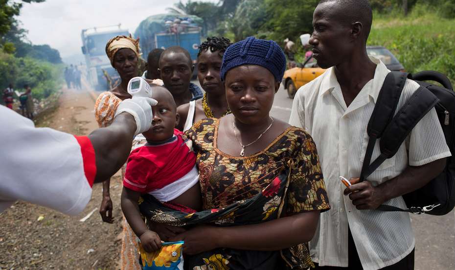Coronavirus in Afrika. Bild: Eine Frau trägt ihr Kleinkind auf dem Arm. Jemand anderes misst, ob das Kind Fieber hat.