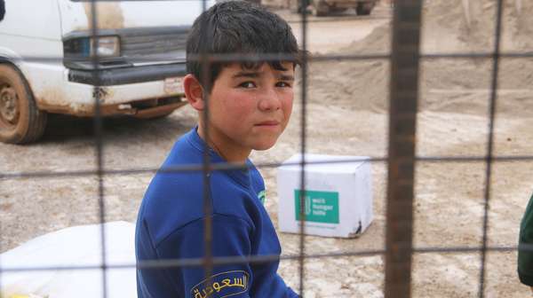 Ein Junge sitzt hinter einem Gitter und schaut in die Kamera. Im Hintergrund steht ein Paket der Welthungerhilfe.