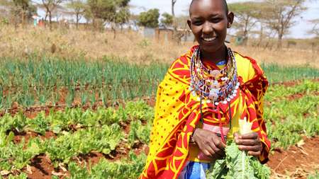 Eine Frau steht mit ihrer Ernte auf dem Feld, Kenia 2020. 