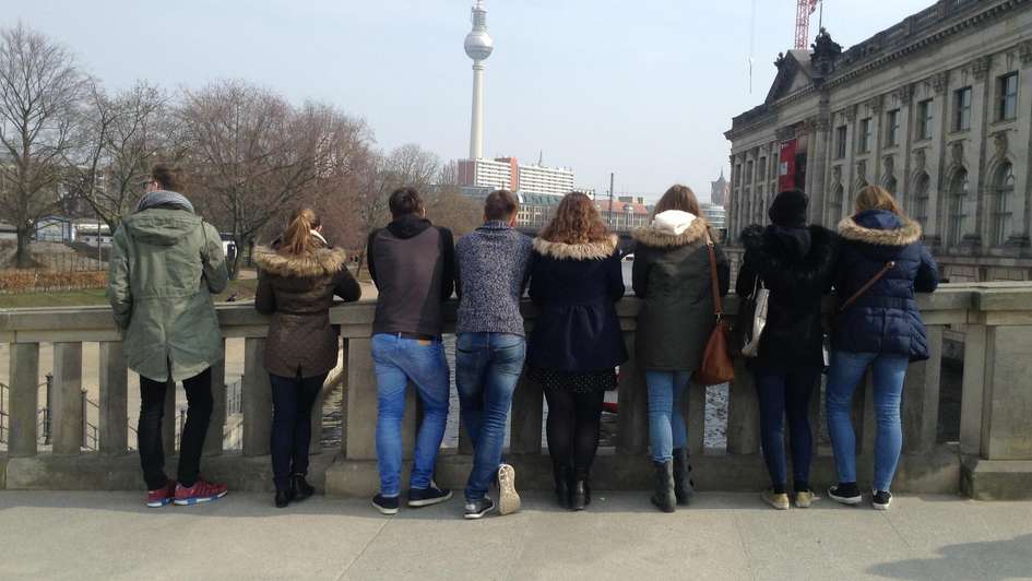 Eine Gruppe von Jugendlichen steht auf einer Brücke und schaut auf Berlin