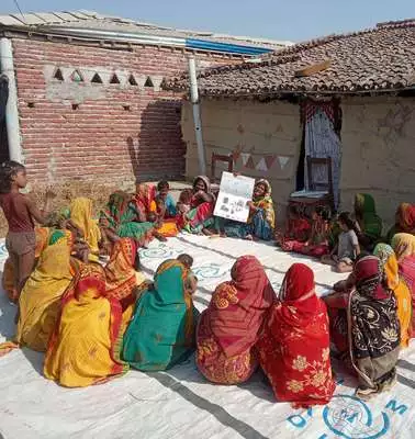 Frauen in Bangladesch sitzen für eine Schulung draußen in einem Kreis und lauschen einer Präsentation