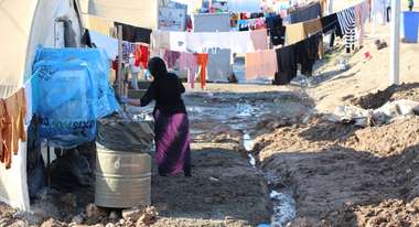 Eine Frau steht vor aufgehangener Wäsche in einem Flüchtlingslager