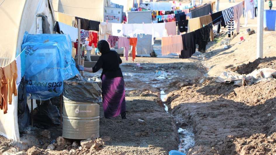 Eine Frau steht vor aufgehangener Wäsche in einem Flüchtlingslager