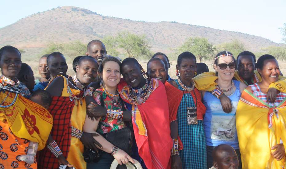 Eine Gruppe von Frauen schaut lachend in die Kamera. Die meisten davon tragen bunte Massaigewänder.