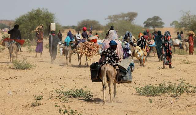 Sudanesische Flüchtlinge, die vor der Gewalt in der Region Darfur geflohen sind, suchen in Goungour, Tschad, vorübergehende Zuflucht. Das Bild zeigt Menschen, die zu Fuß und mit Eseln unterwegs sind und Gepäck tragen.