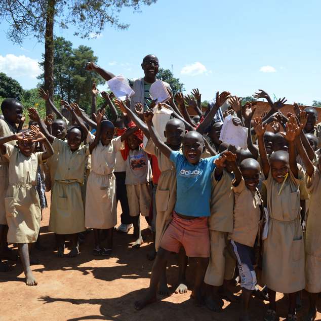 Eine Gruppe jubelnder Kinder steht mit ihrem Lehrer vor ihrer Grundschule.