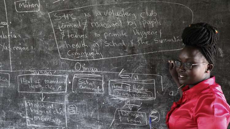 Bildung im Südsudan. Eine Lehrerin steht vor einer mit Kreide beschriebenen Schultafel