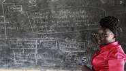 Bildung im Südsudan. Eine Lehrerin steht vor einer mit Kreide beschriebenen Schultafel