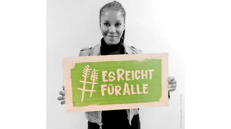 Schauspielerin Liz Baffoe hält ein Schild mit dem Welthungerhilfe-Hashtag #EsReichtFürAlle.