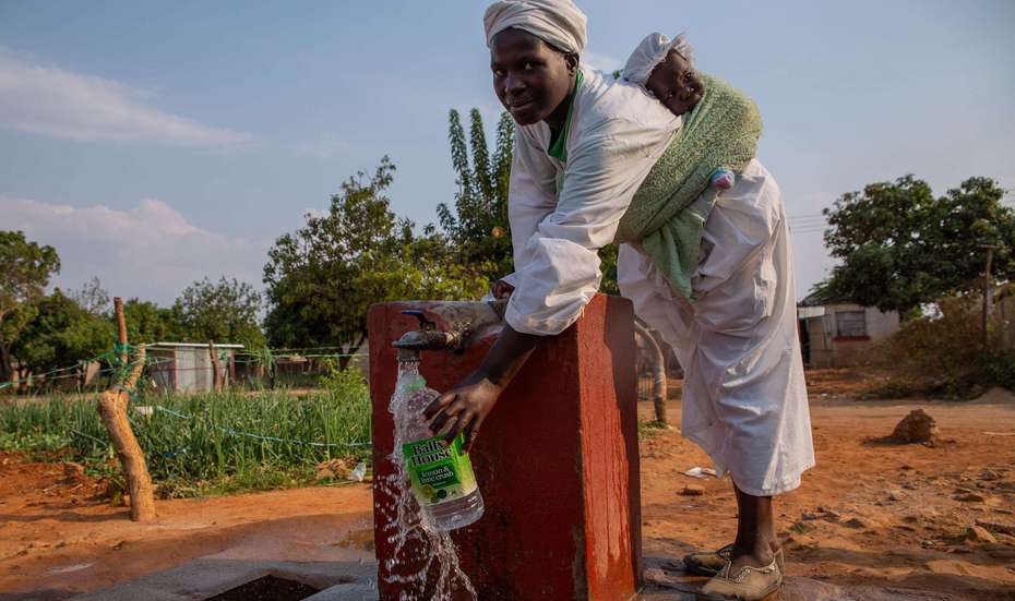 Schutz gegen das Coronavirus: Regelmäßiges Händewaschen. Bild: Eine Frau mit einem Baby auf dem Rücken holt Wasser an einem Brunnen.