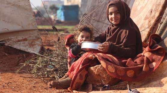 Frau und Kind essen vor Zelt in Syrien. 