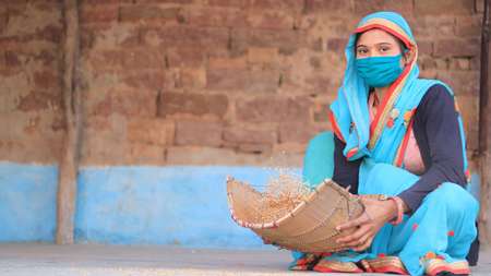Eine Frau mit Mundschutz sitzt auf dem Boden und siebt Getreide.