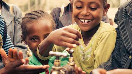 Lachende Kinder stehen um einen Wasserhahn herum und waschen sich die Hände, Äthiopien 2017.