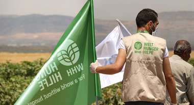 Ein Mann mit Welthungerhilfe-Weste hält eine grüne Flagge mit dem neuen Welthungerhilfe-Logo in der Hand.