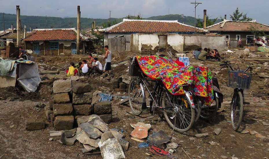 Menschengruppen sitzen in den Trümmern ihrer Häuser.