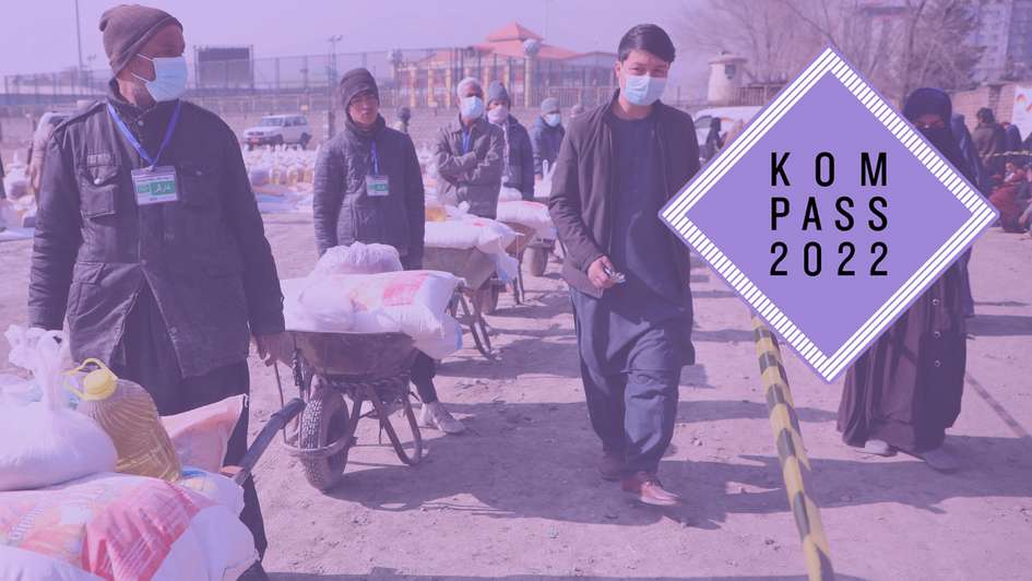 Lebensmittelverteilung in Kabul, Afghanistan. Männer schieben Schubkarren mit Nahrungsmitteln. Oben rechts ist das Logo des Kompass 2022 auf dem Bild.