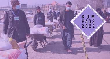 Lebensmittelverteilung in Kabul, Afghanistan. Männer schieben Schubkarren mit Nahrungsmitteln. Oben rechts ist das Logo des Kompass 2022 auf dem Bild.