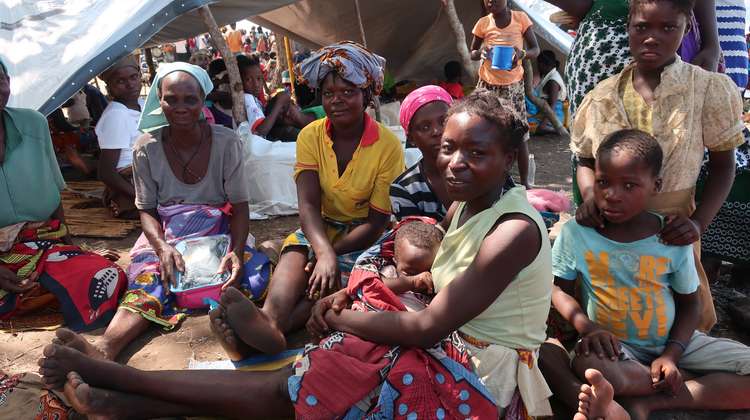 Drei Frauen und fünf Kinder sitzen vor einer Plane, die als Notunterkunft aufgespannt wurde.