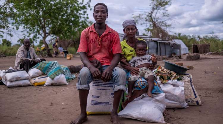 Eine Frau mit einem Kind auf ihrem Schoß und ein Mann sitzen auf Hilfsgüter-Säcke.