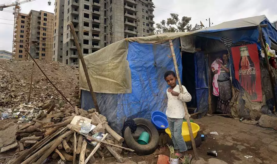 Bevölkerungswachstum in den Städten. Bild: Ein Kind steht vor einer aus Planen und Holz gebauten provisorischen Unterkunft.