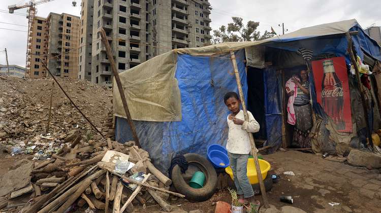 Bevölkerungswachstum in den Städten. Bild: Ein Kind steht vor einer aus Planen und Holz gebauten provisorischen Unterkunft.