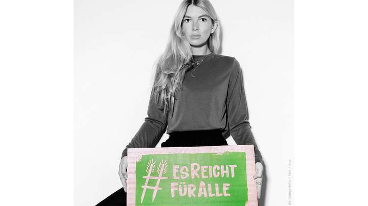 Fotografin Kim Alena hält ein Schild mit dem Welthungerhilfe-Hashtag #EsReichtFürAlle.