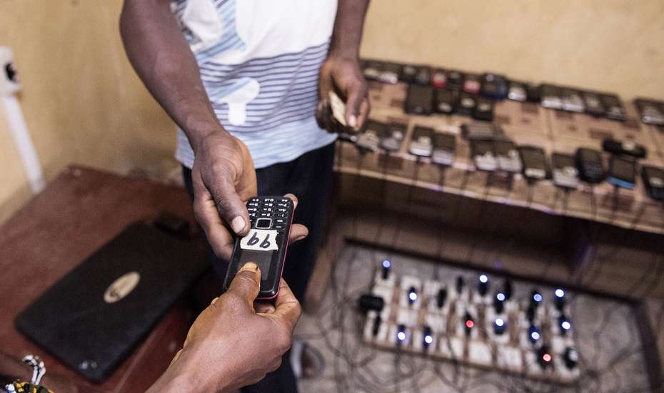 Ein Mann nimmt sein aufgeladenes Handy an einer Aufladestation in Sierra Leone in Empfang.