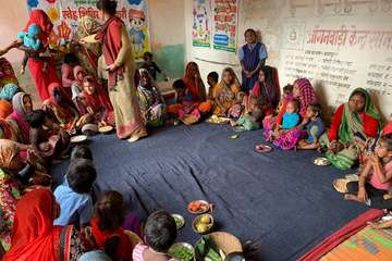 Nutrition Smart-Dorf in Indien: Frauen und Kinder sitzen in einem Kreis und lernen, wie man sich ausgewogen ernährt.