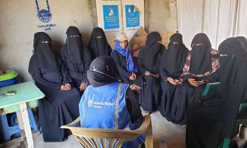 Eine Hilfsarbeiterin von Islamic Relief sitzt mit dem Rücken zur Kamera vor einer Gruppe verschleierter Frauen bei einer Schulung.
