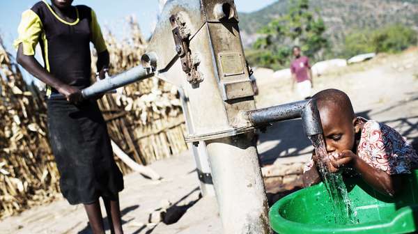 Jetzt für Malawi spenden. Bild: Junge trink Wasser an einem Brunnen.