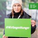 Anja Kling hält ein grünes Schild, darauf steht: #WirGegenHunger