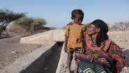 Vor einer ausgetrockneten Landschaft in Äthiopien steht eine Mutter mit ihrem kleinen Sohn.