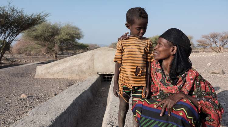 Vor einer ausgetrockneten Landschaft in Äthiopien steht eine Mutter mit ihrem kleinen Sohn.