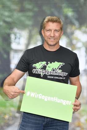Marko Rehmer hält ein grünes Schild in der Hand, darauf steht: #wirgegenhunger.