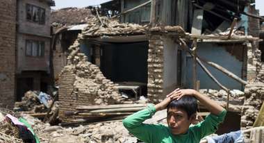 A boy in the front. Behind him a destroyed house.