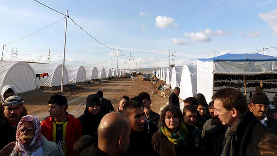 Eine Gruppe von Flüchtlingen in einem Flüchtlingslager ist im Gespräch mit Wolfgang Jamann