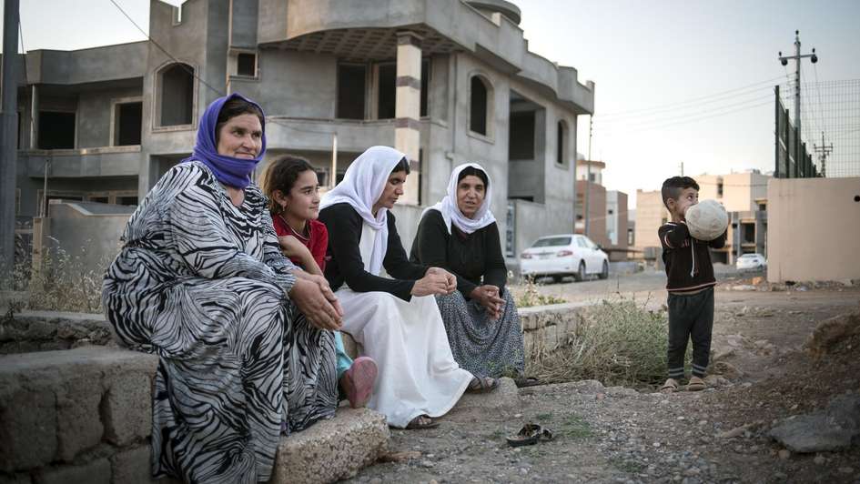 Eine Gruppe jesidischer Flüchtlinge sitzt innerhalb einer Siedlung von Hausrohbauten